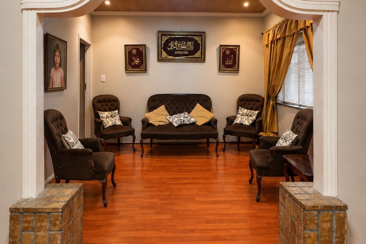 A formal living room featuring a decorative arched entryway with stone-clad pillars, wood-look laminate flooring, and recessed ceiling lighting.