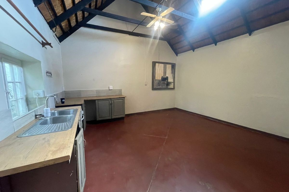 An empty kitchen featuring a high vaulted ceiling with exposed timber rafters, fitted cabinetry, and a stainless steel double sink.