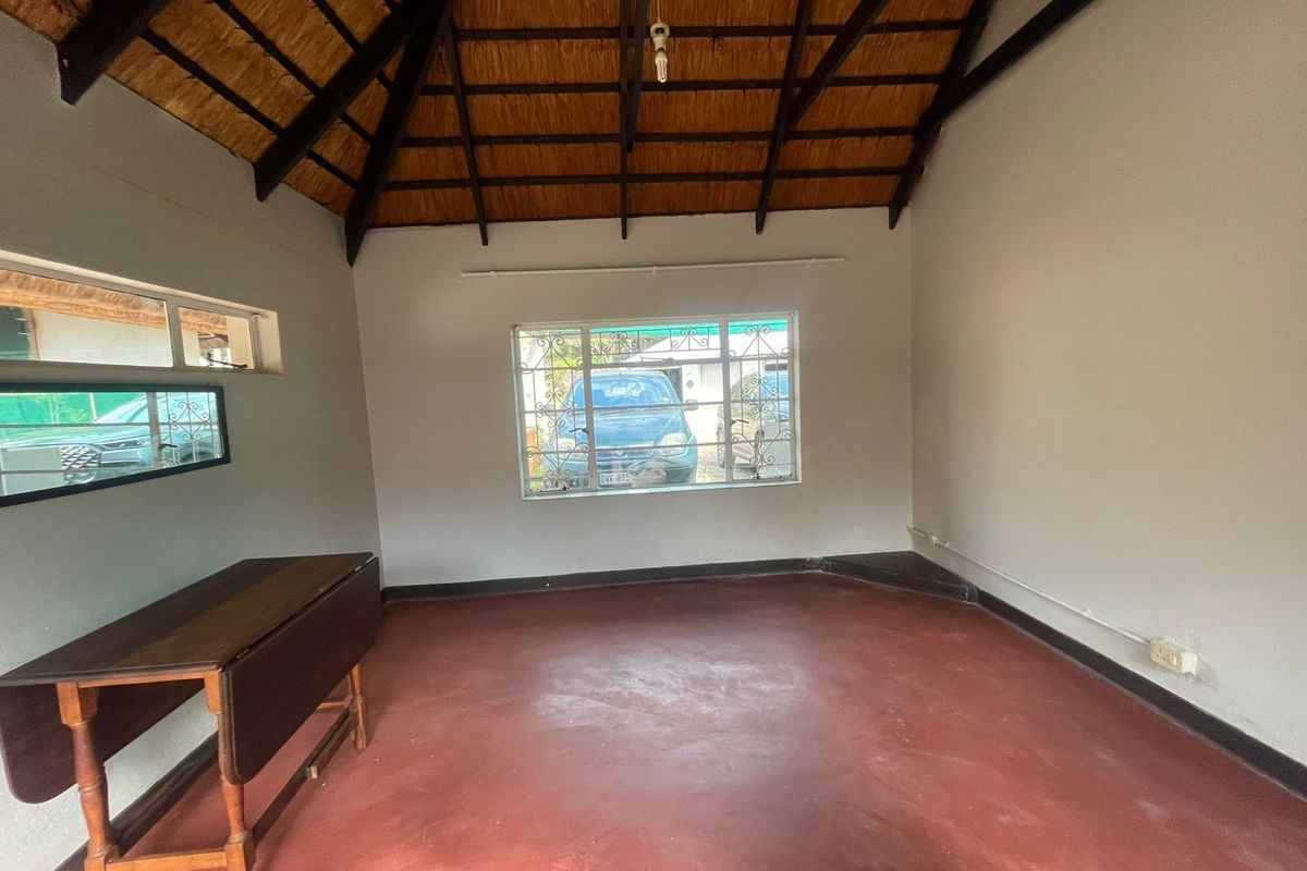 Empty living room featuring a high exposed thatch ceiling with timber rafters, painted concrete flooring, and steel-framed windows with security bars.