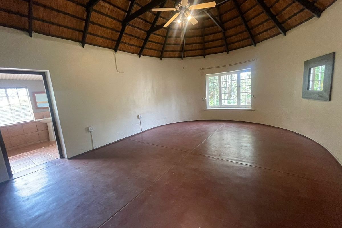 Spacious circular bedroom featuring a high thatched roof with exposed timber rafters, a ceiling fan, and polished screeded concrete flooring.
