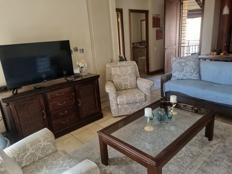 A comfortable living room area featuring tiled flooring, neutral wall tones, and direct access to an adjacent hallway and outdoor balcony space.