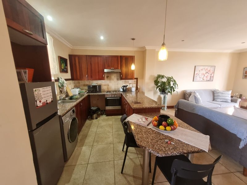 Open-plan kitchen featuring granite countertops, wooden cabinetry, built-in oven, hob, and extractor fan, seamlessly flowing into the adjacent living area.