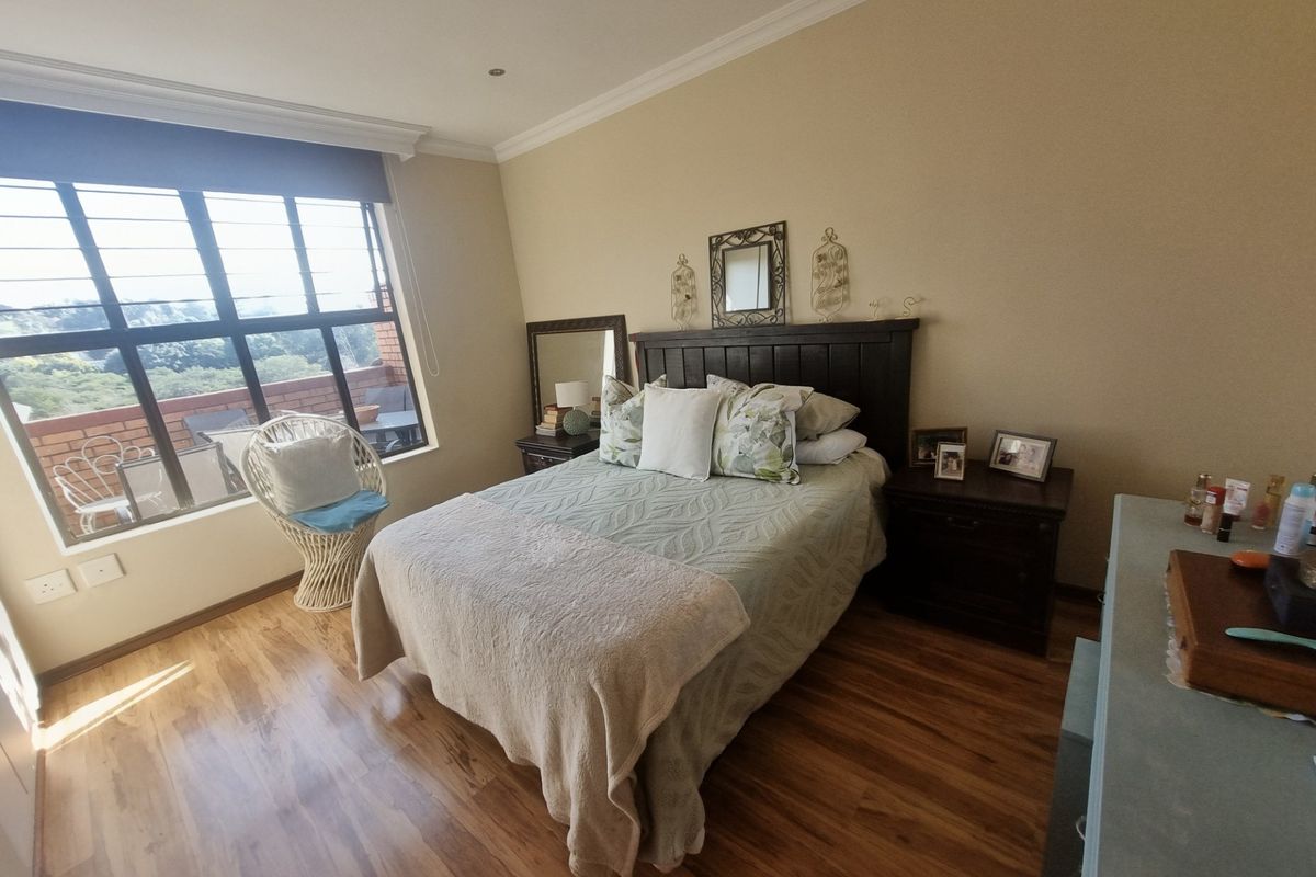 A well-lit bedroom featuring wood-look flooring, large windows with security bars, and access to an adjoining balcony.
