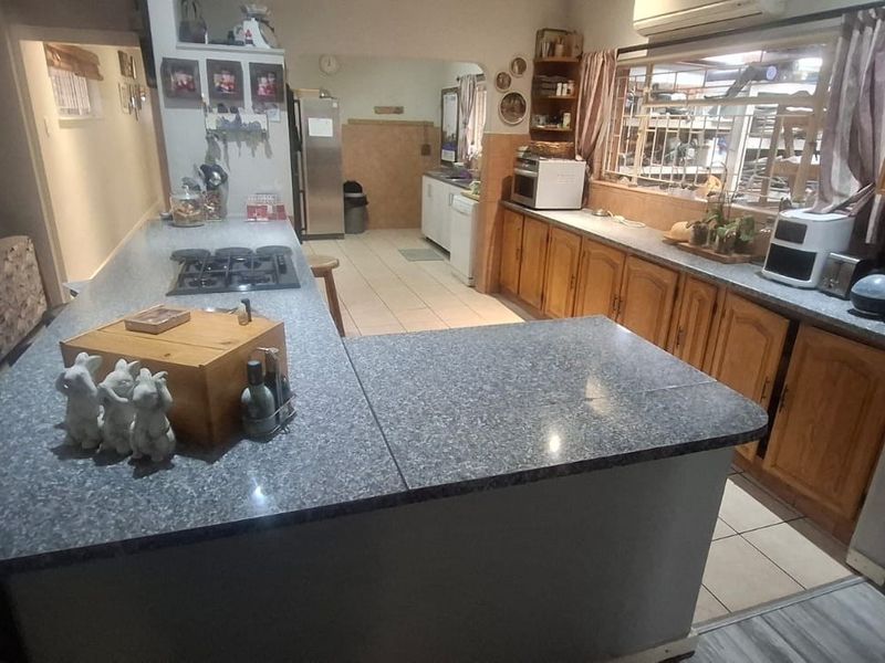 Open plan kitchen featuring a large central island with integrated gas hob, ample wooden cabinetry, and tiled flooring, connecting to the adjacent living area.