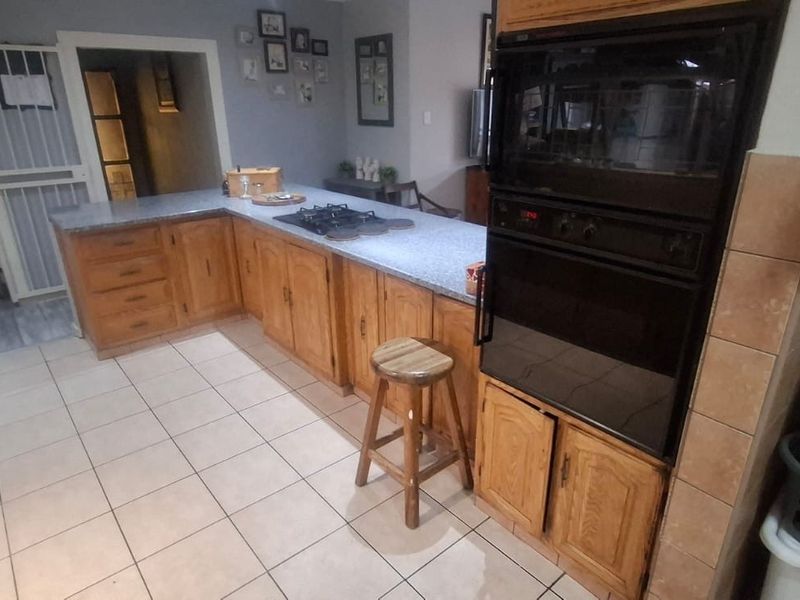 A functional kitchen featuring wooden cabinetry, a built-in double oven, gas hob, and tiled flooring, providing a practical layout for daily meal preparation.