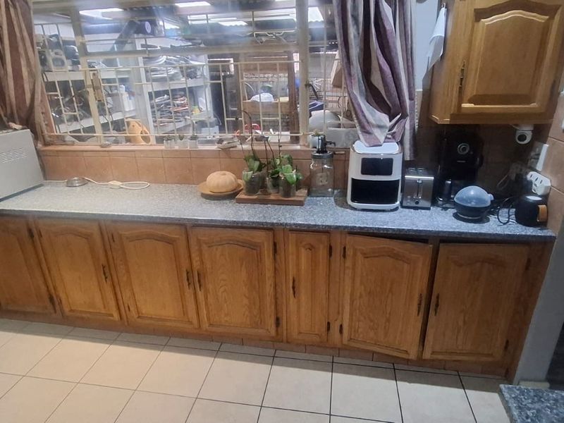 A functional kitchen featuring traditional timber cabinetry, laminate countertops, and tiled flooring, with a large window providing natural light.