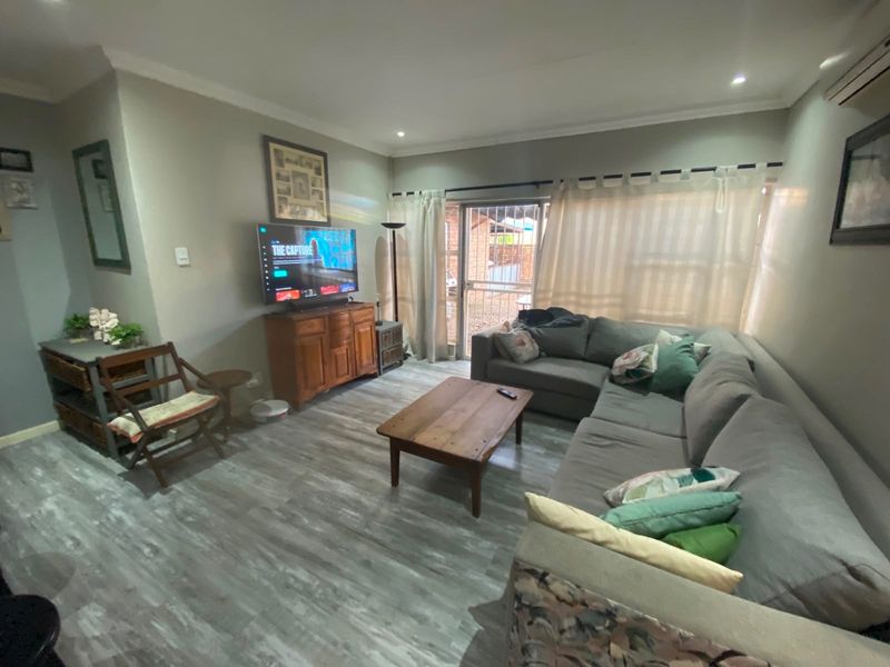 A comfortable living room featuring modern wood-look flooring, recessed ceiling lighting, and a sliding glass door providing access to the outdoor area.
