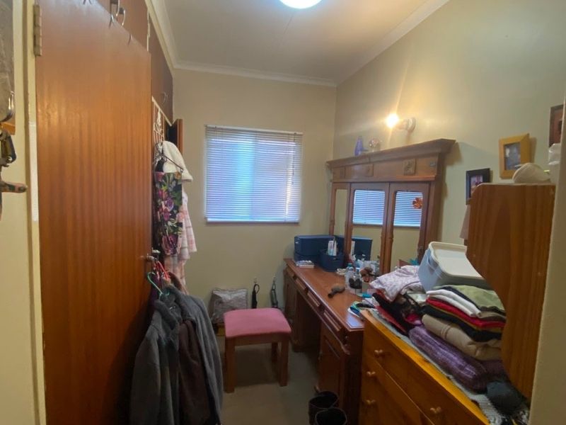 A functional bedroom featuring built-in wooden cabinetry and a window with fitted blinds, offering a practical layout for storage and personal use.