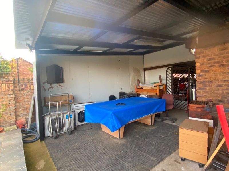 A covered outdoor patio area featuring a corrugated metal roof, exposed brick walls, and concrete flooring, suitable for an entertainment or utility space.