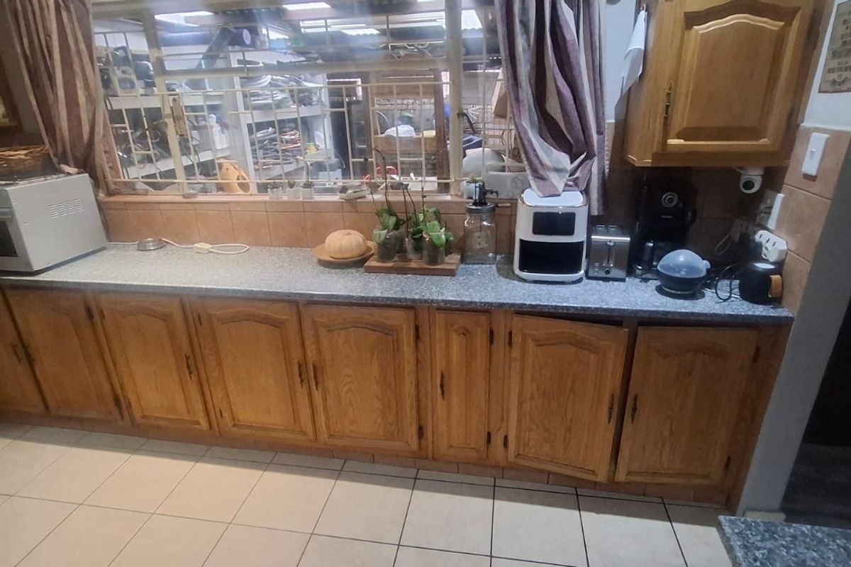 A functional kitchen featuring traditional timber cabinetry, laminate countertops, and tiled flooring, with a large window providing natural light.