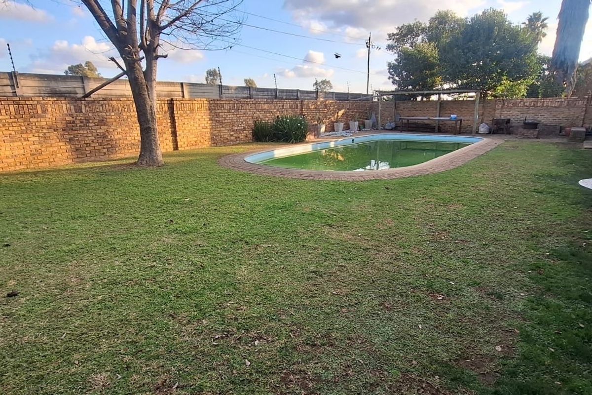 Rear garden featuring a swimming pool, brick boundary wall, and lawn area, providing a private outdoor space for the property.