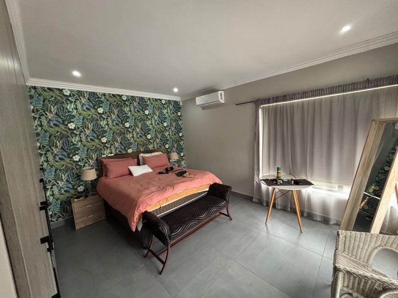 Spacious bedroom featuring tiled flooring, recessed downlighting, air conditioning, and a decorative feature wall with built-in cupboard storage.