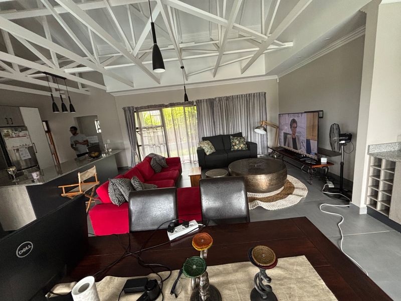 Spacious open-plan living area featuring exposed white roof trusses, a modern kitchen with granite island, and tiled flooring throughout.