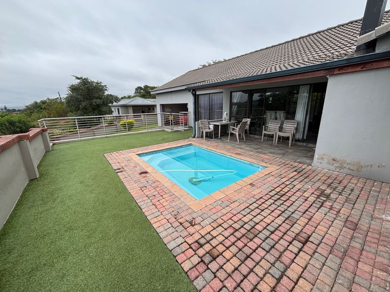 Outdoor pool area featuring a small swimming pool, brick paving, artificial lawn, and a covered patio with sliding door access to the home.