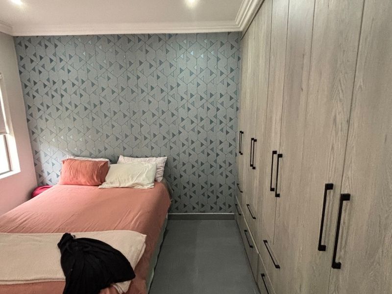 A well-maintained bedroom featuring extensive built-in cupboards with modern hardware, recessed downlighting, and decorative feature wallpaper.