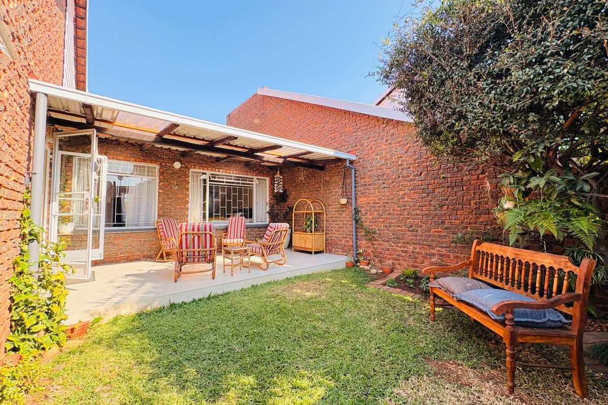 A private rear garden featuring a paved patio area with a covered pergola, brick boundary walls, and established greenery.