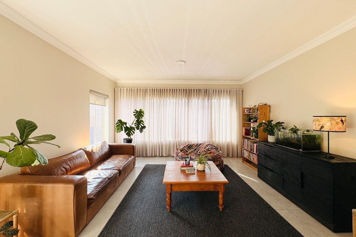 A bright and spacious living room featuring tiled flooring, crown molding, and large windows with floor-to-ceiling curtains providing ample natural light.