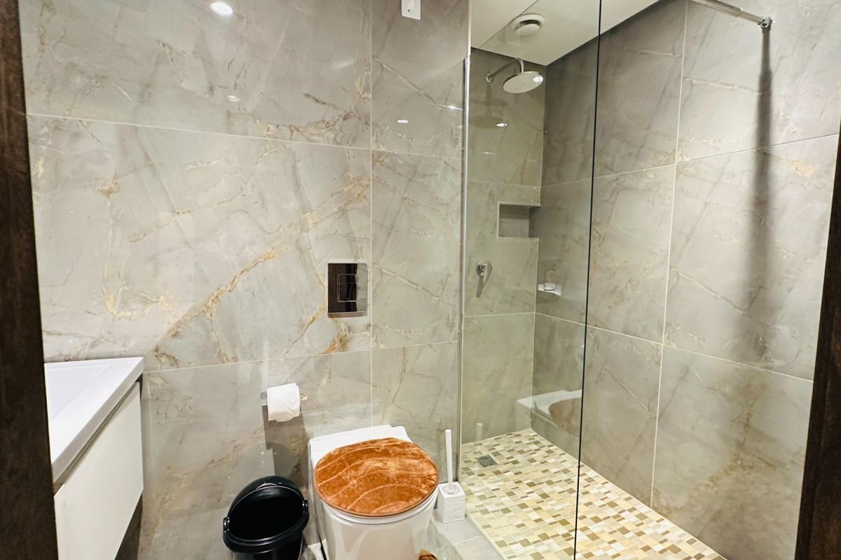 Modern bathroom featuring large-format marble-look wall tiles, a glass-enclosed walk-in shower with mosaic floor tiling, and a wall-mounted toilet.