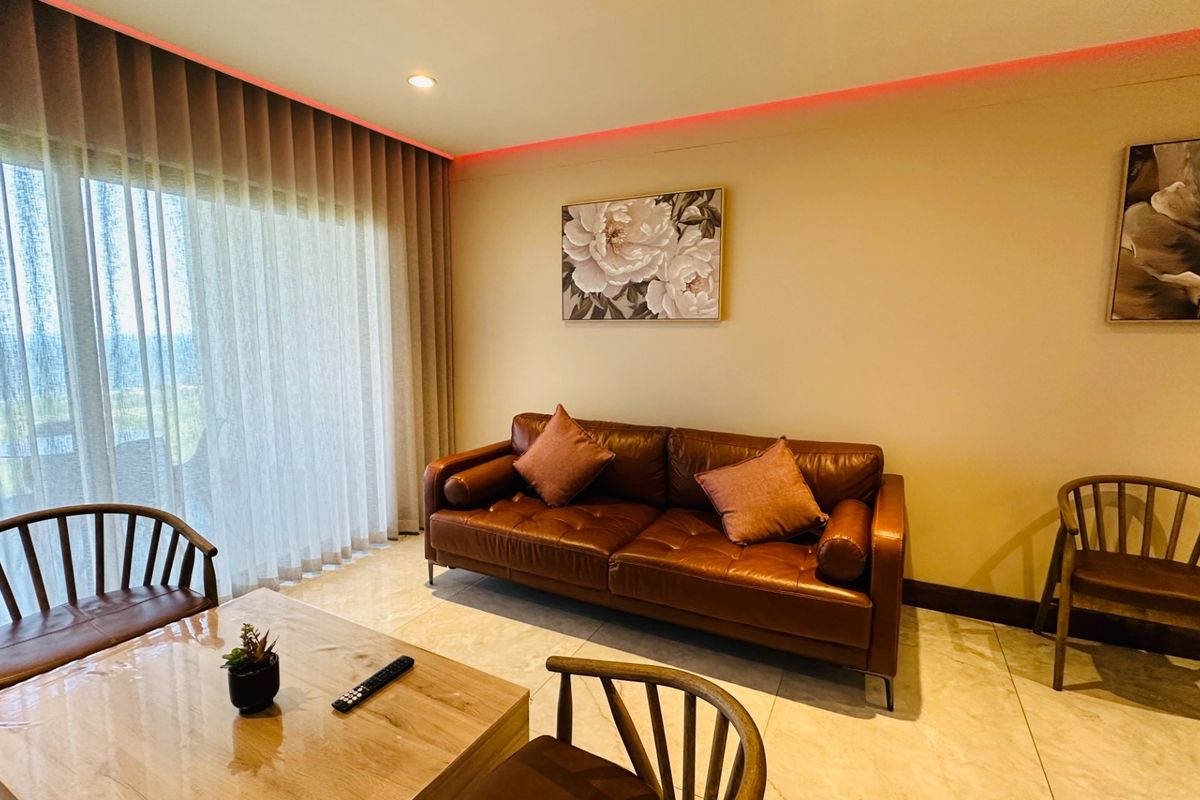 A well-maintained living room featuring large floor-to-ceiling windows with sheer curtains, recessed ceiling lighting, and polished tile flooring.
