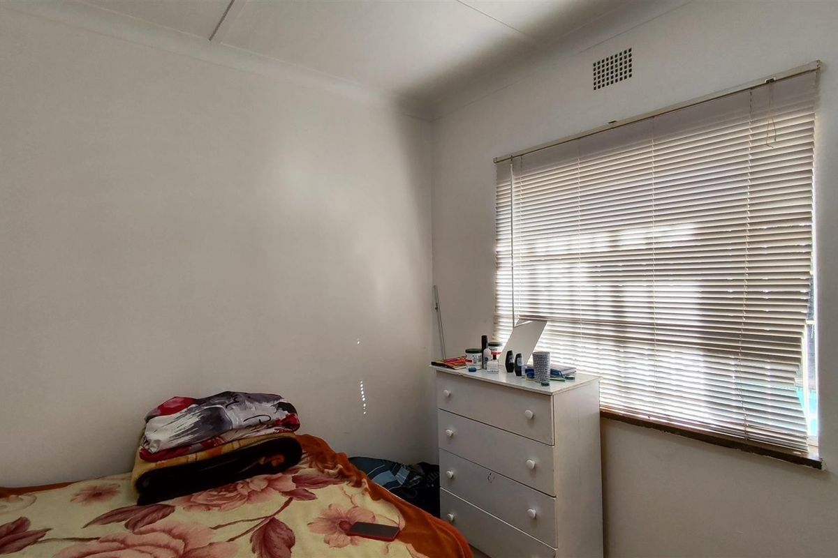 A standard bedroom featuring a window with fitted horizontal blinds and a ceiling ventilation vent.