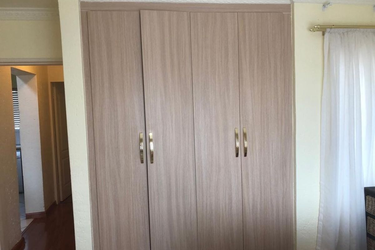 A bedroom featuring built-in wooden wardrobes with modern handles and decorative crown molding.