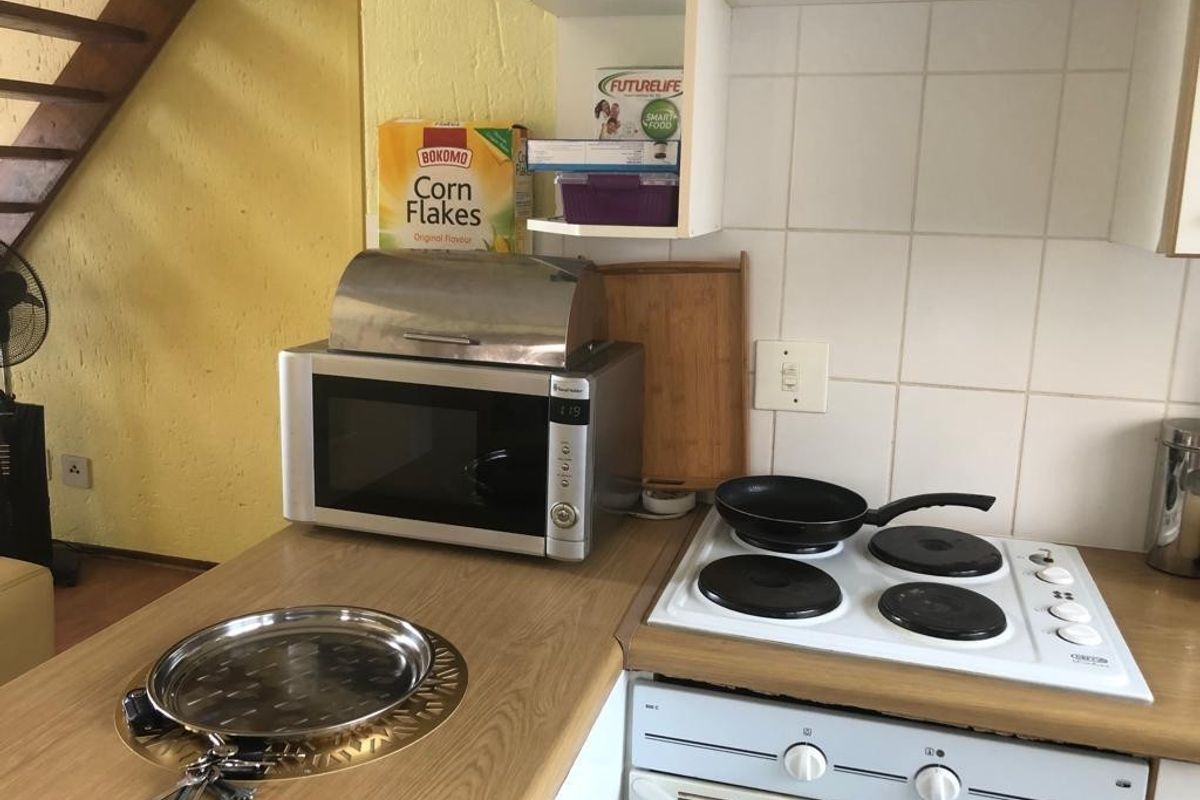 Compact kitchen area featuring a built-in electric hob, oven, and laminate countertops, situated adjacent to an open staircase.