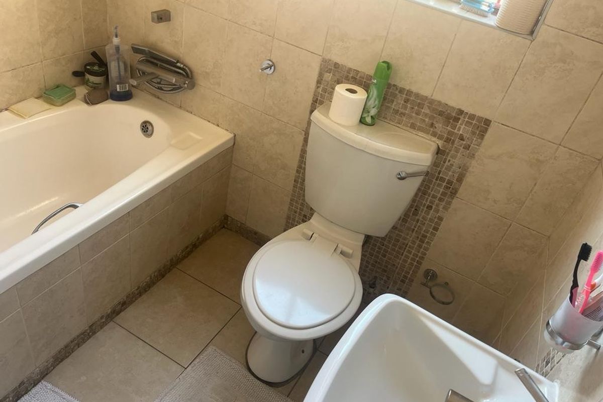 A functional bathroom featuring a built-in bathtub, a standard toilet, and a wall-mounted basin with tiled walls and flooring.