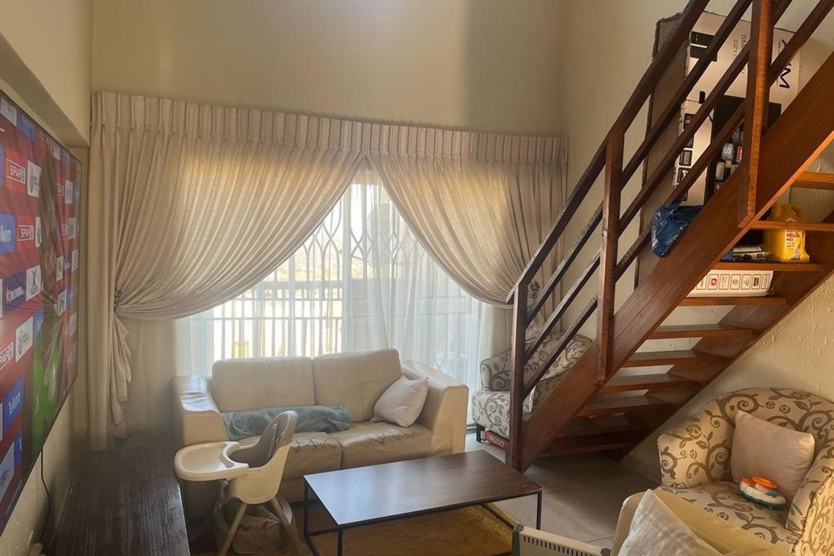 Living room featuring high ceilings, a wooden staircase, and large sliding doors with security gate, providing access to the outdoor area.