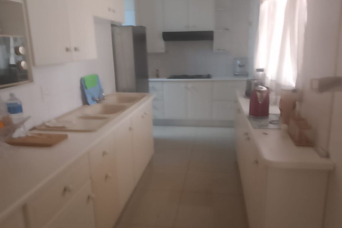 A functional galley-style kitchen featuring white cabinetry, integrated cooktop, extractor fan, and double basin sink with tiled flooring.