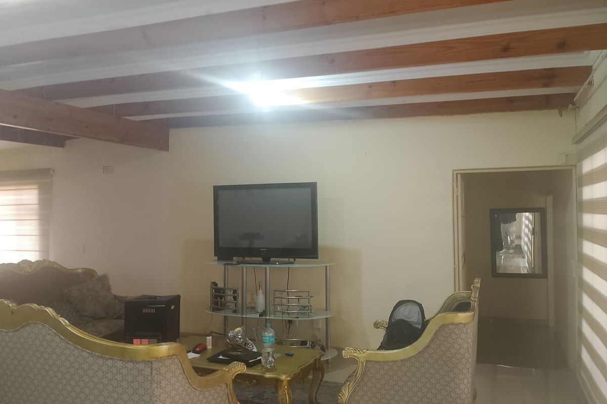 A living room featuring exposed timber ceiling beams and tiled flooring, providing a functional space with natural light from the side windows.