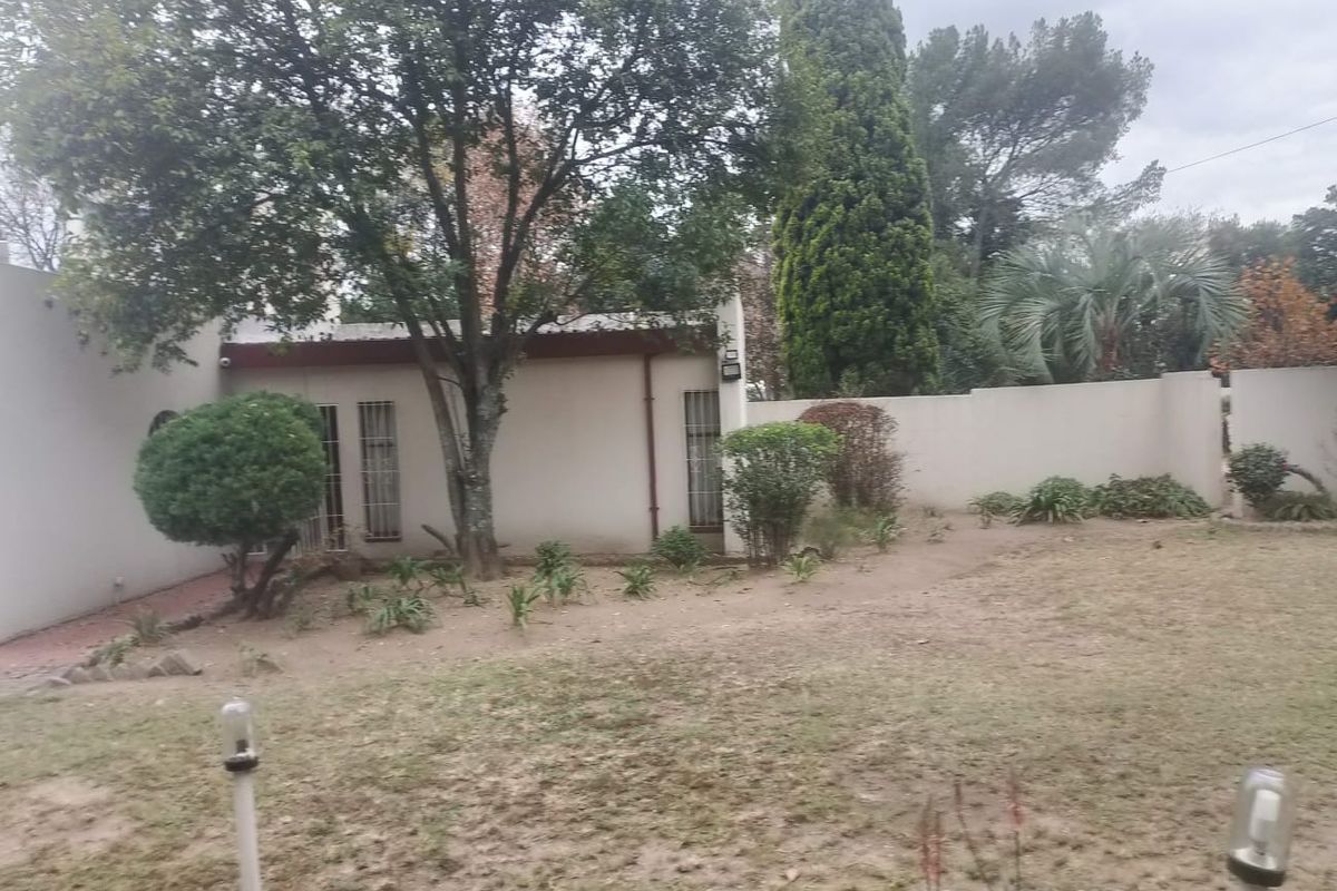 A view of the rear garden area featuring established trees, perimeter walling, and a section of the house exterior with security bars.