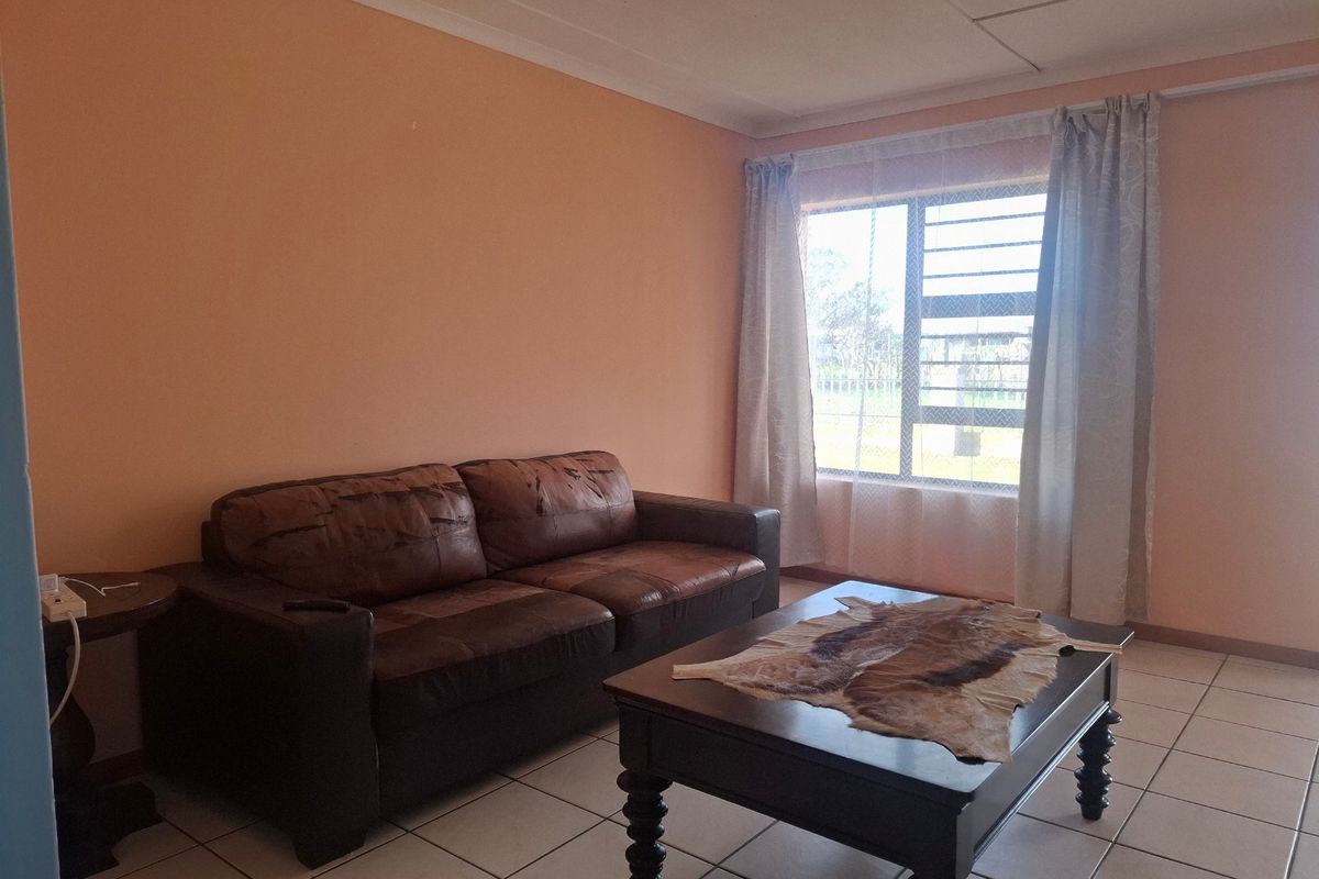 A living room featuring tiled flooring, a large window with security bars, and coved ceilings, requiring cosmetic updates to improve the overall aesthetic.