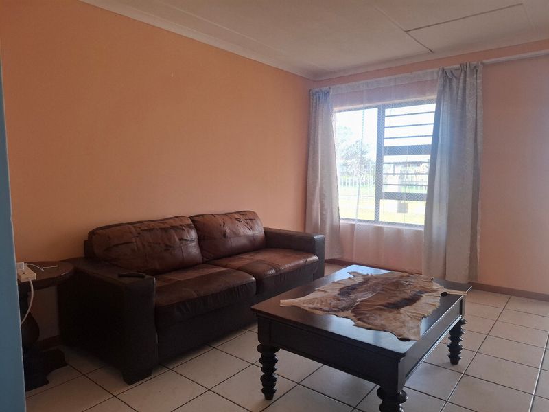A living room featuring tiled flooring, a large window with security bars, and coved ceilings, requiring cosmetic updates to improve the overall aesthetic.