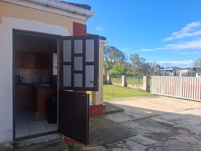 Rear view of the property showing a concrete driveway, metal gate, and access to a small kitchen area with cabinetry and tiled flooring.