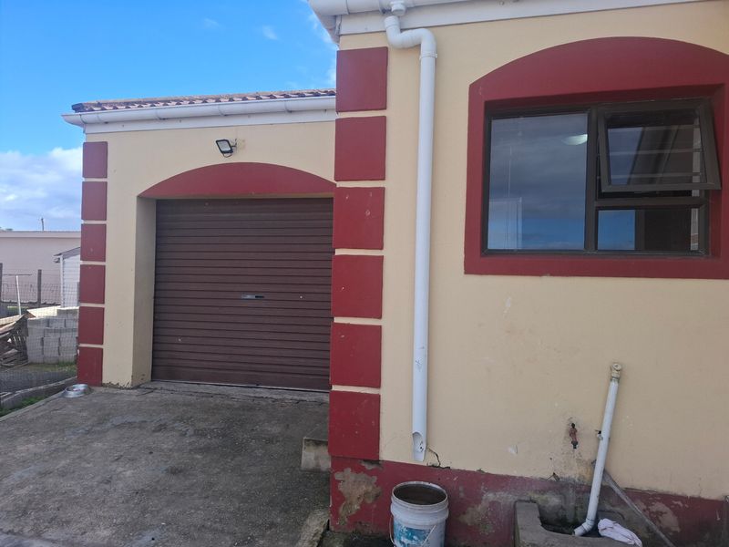 Exterior view of a residential garage with a roller door, showing visible wear to the exterior wall plaster and paintwork.