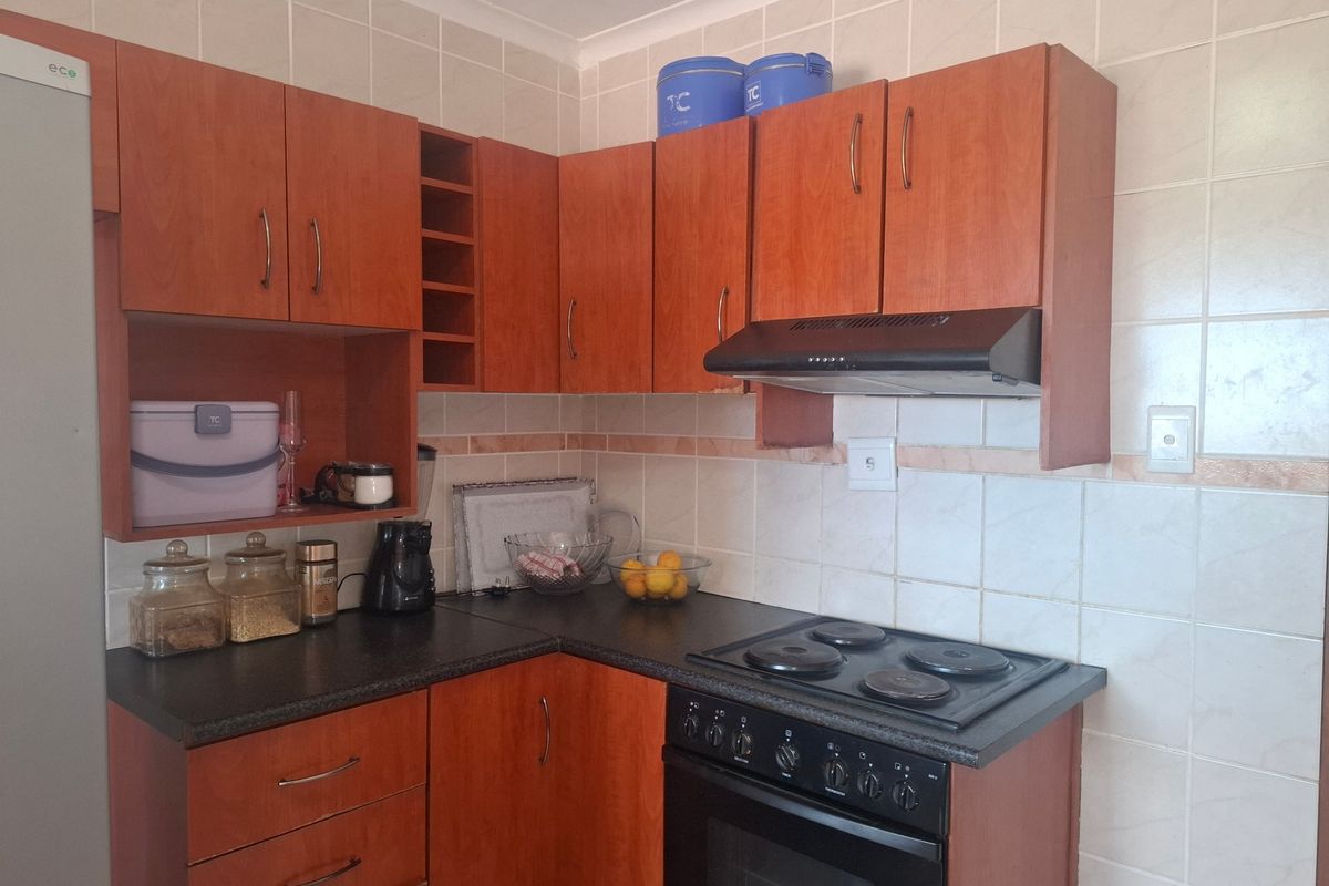 A functional kitchen featuring wood-look laminate cabinetry, dark countertops, ceramic wall tiling, and a built-in electric oven with a hob and extractor fan.