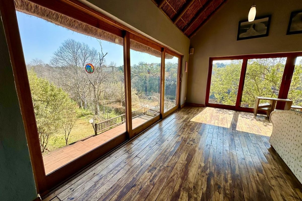 Spacious living area featuring warm timber flooring, exposed thatch roof rafters, and expansive sliding glass doors offering scenic views of the surrounding landscape.