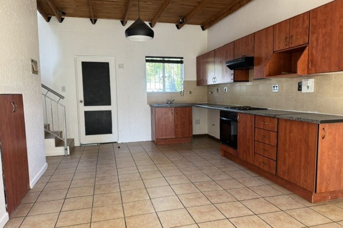 Spacious kitchen featuring wooden cabinetry, built-in oven and hob, tiled flooring, and exposed wooden ceiling beams, with an adjacent staircase.