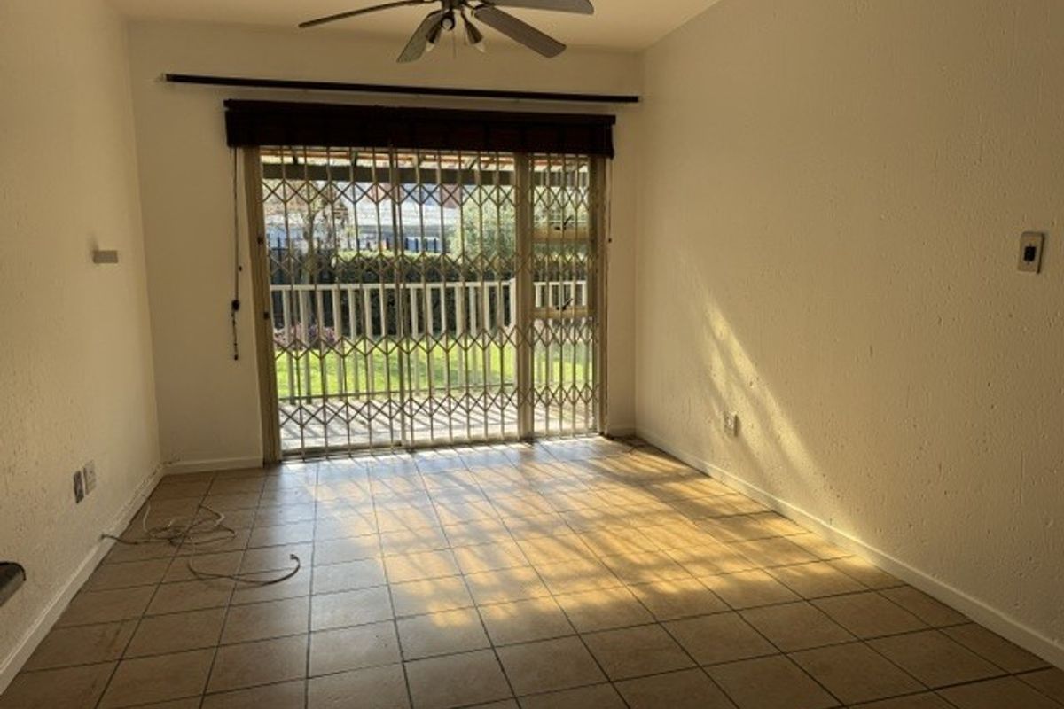 An empty living room featuring tiled flooring, a ceiling fan, and a sliding glass door with a security gate leading to the exterior.