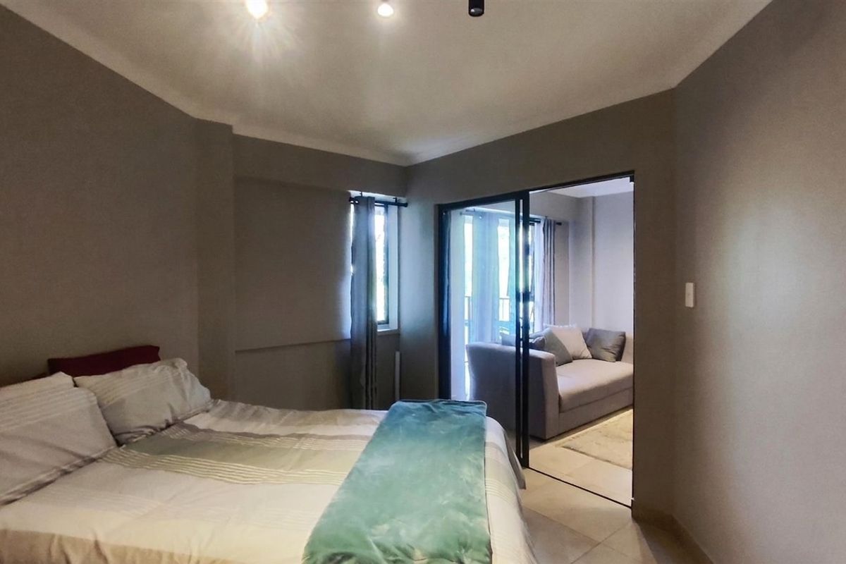 A well-maintained bedroom featuring neutral wall tones, recessed ceiling lighting, and a sliding glass door leading to an adjacent living area.