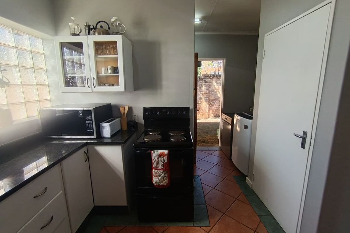 Functional kitchen featuring dark granite countertops, white cabinetry, a freestanding stove, and a glass block window, with direct access to an outdoor area.