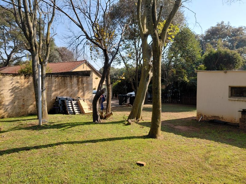 A view of the rear garden area featuring mature trees, lawn space, and exterior walls of the farm outbuildings.