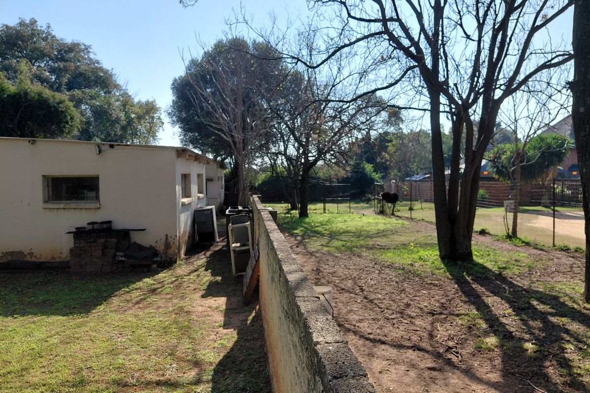 Exterior view of a farm property featuring a masonry boundary wall, mature trees, and a side elevation of a building with weathered plaster finishes.