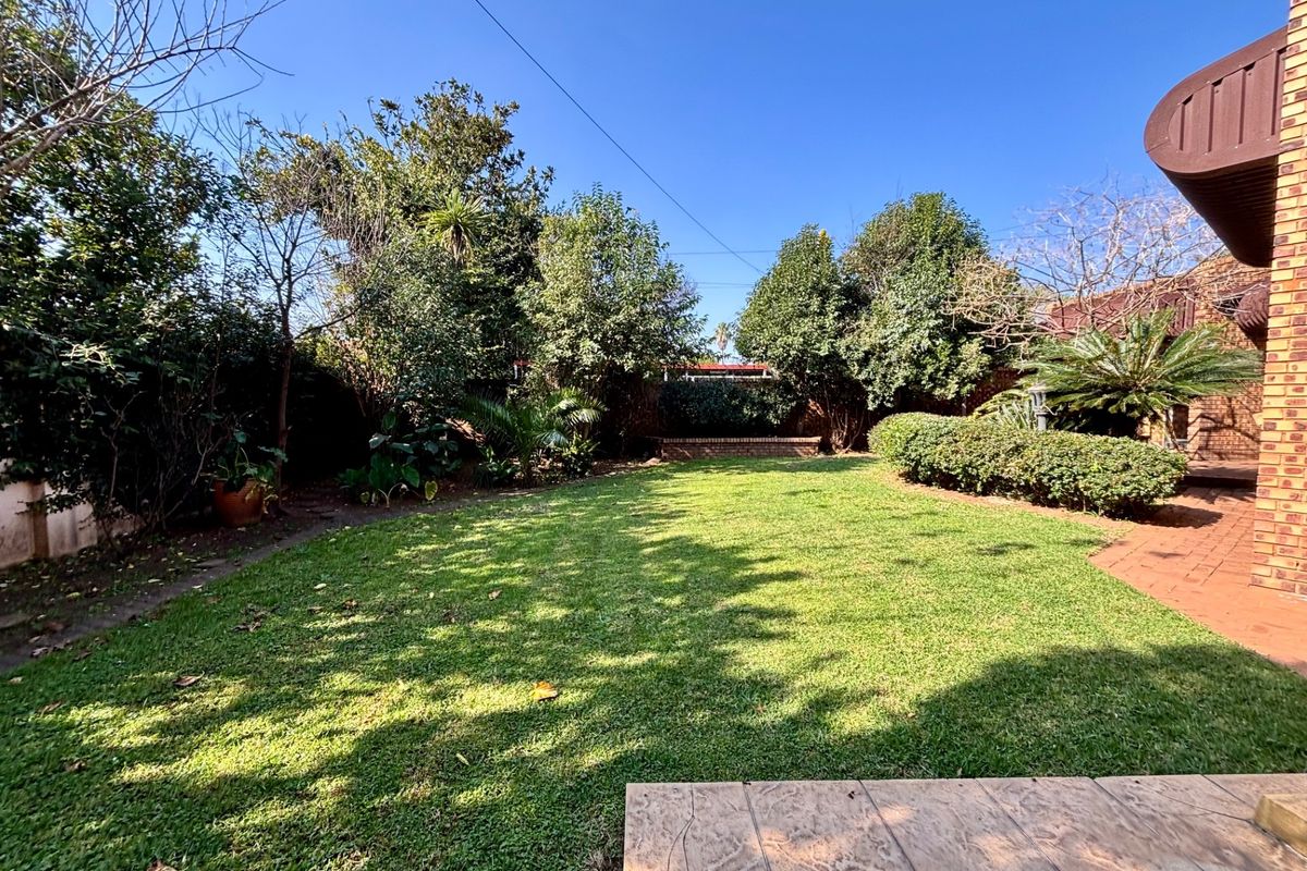 A private rear garden featuring a well-maintained lawn, mature trees, established shrubbery, and a paved patio area adjacent to the brick-built house.