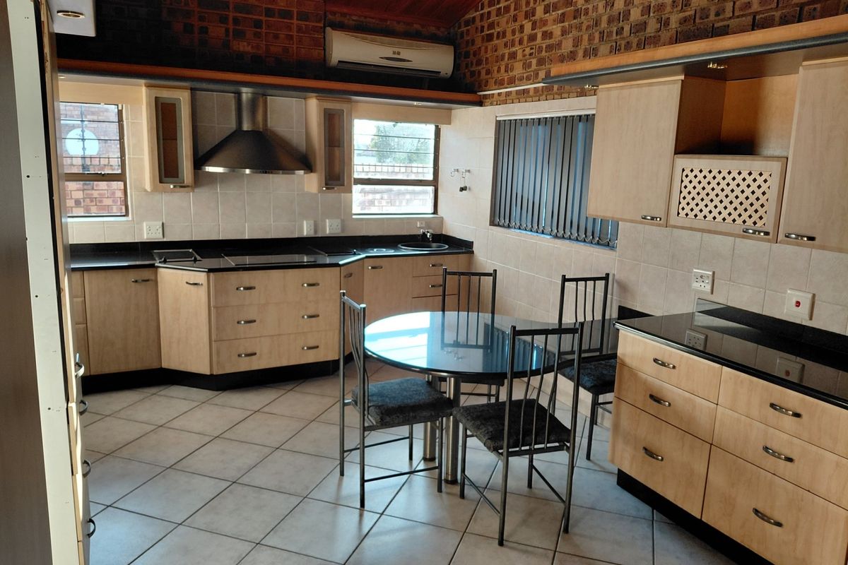 Spacious kitchen featuring light wood cabinetry, dark granite countertops, tiled flooring, stainless steel extractor fan, and a dedicated dining area.