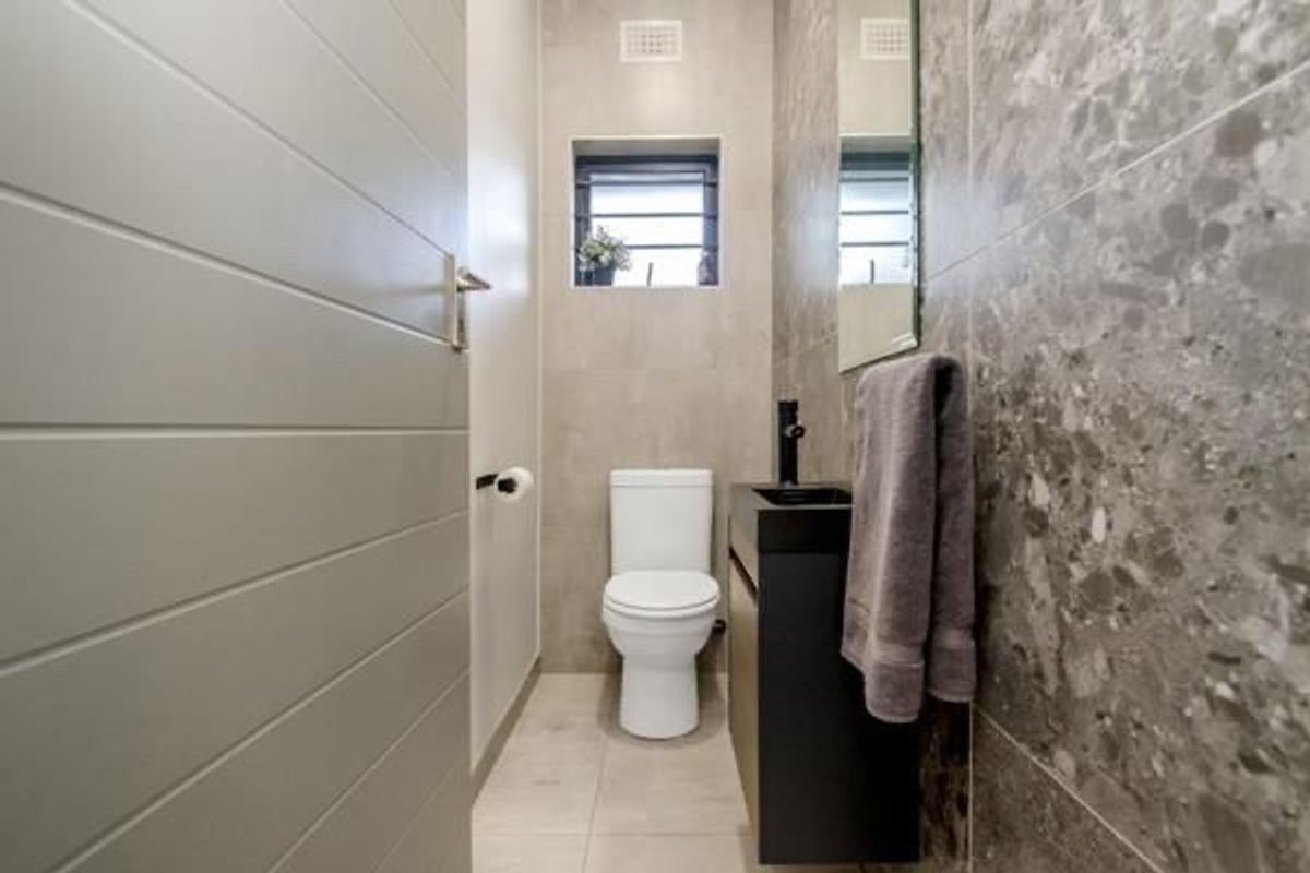 Modern guest bathroom featuring contemporary grey tiling, a sleek vanity with a black basin, and a wall-mounted toilet.