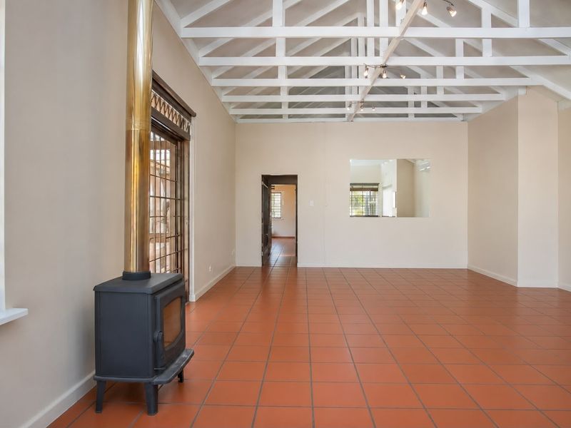 Spacious living area featuring high vaulted ceilings with exposed beams, terracotta floor tiles, and a built-in fireplace with a metallic flue.