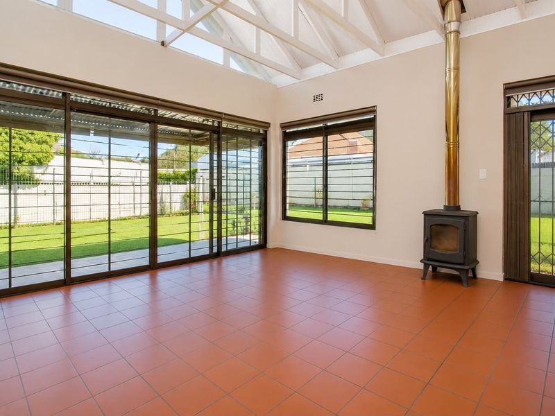 Spacious living area featuring terracotta tiled flooring, a freestanding fireplace, vaulted ceilings, and large sliding glass doors providing access to the garden.