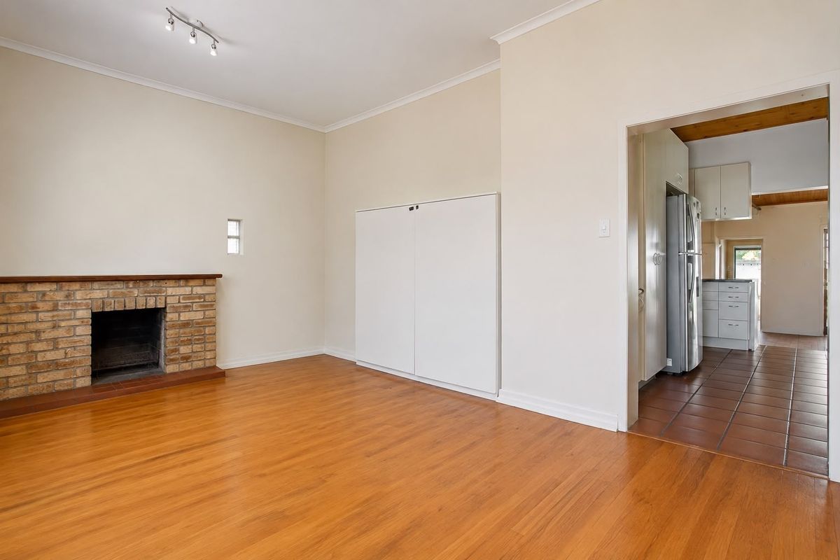 A bright living room featuring a brick fireplace and wood-look flooring, with an adjacent kitchen area visible through the doorway.