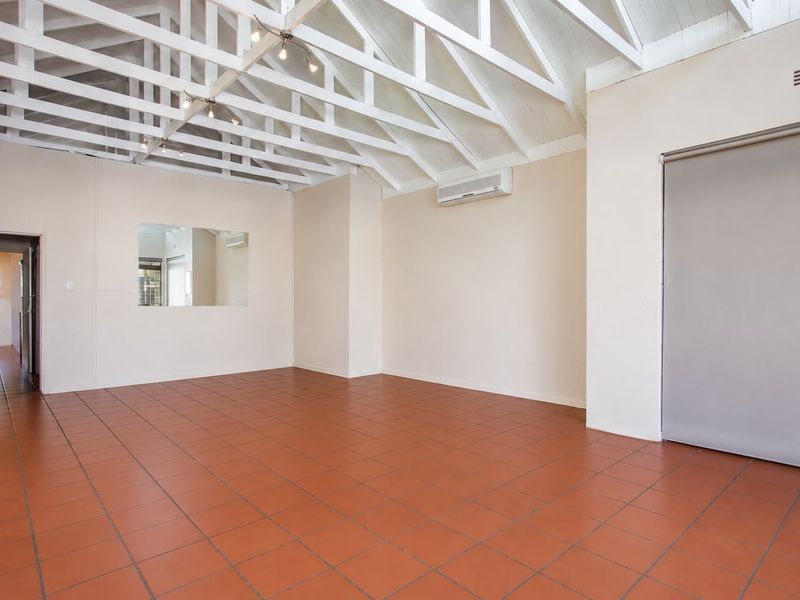 Spacious open-plan area featuring high vaulted ceilings with exposed trusses, terracotta tiled flooring, and a wall-mounted air conditioning unit.